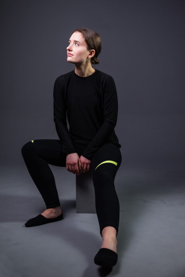 A white woman is sitting while modeling activewear in black and lime.